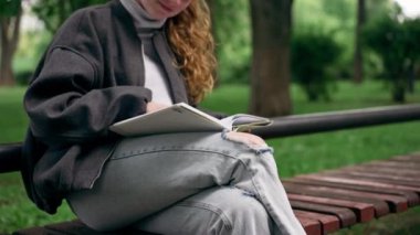 Parkta, siyah ceketli, saçları birbirine dolanmış, yalnız bir kız kitap okuyor.