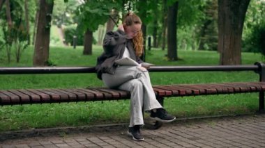 Parkta siyah ceketli, saçları birbirine dolanmış, yalnız bir kız bir bankta oturmuş kitap okuyor.