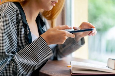 Pencerenin yanındaki bir kitapçıda güzel bir öğrenci oturmuş kitap okuyor sınavlara hazırlanıyor ve pencerenin önünde cep telefonuyla fotoğraf çekiyor.