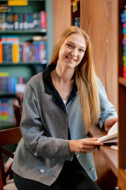 Pencerenin yanındaki bir kitapçıda güzel bir öğrenci oturmuş kitap okuyor kameraya gülümseyen sınavlara hazırlanıyor.