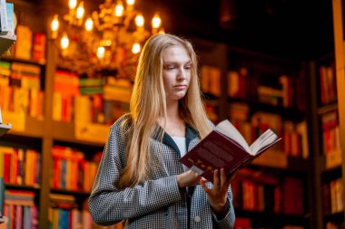 Güzel bir kitapçıda, uzun saçlı genç bir kız öğrenim yıllarında kitaplıkların arasında kitap okuyor.