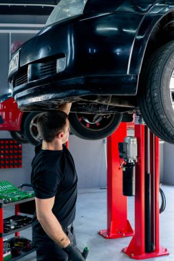 Benzin istasyonundaki oto tamircisi asansörde kaldırılan bir arabayı kontrol eder, mekanik bir araçla arıza düzeltir motor alt gövdenin bir parçasıdır