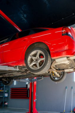 Bir otomobil tamircisi için özel bir mekanizma tarafından bir benzin istasyonunda tekerlekleri yükseltilmiş kırmızı bir arabanın yakın çekimi.