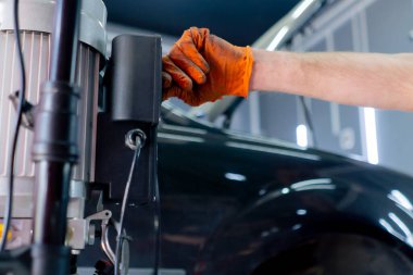 Bir araba servisinde yakın plan bir tamirci şasiyi onarmak için asansör düğmesine basar.