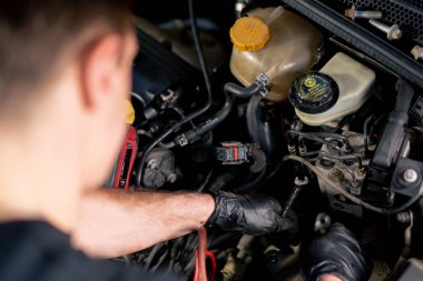 Bir araba servisi merkezinde siyah tişörtlü bir usta araç gereçleri kullanarak motor vidalarını söker yedek parçaların yerine yedek parçaları yerleştirir.