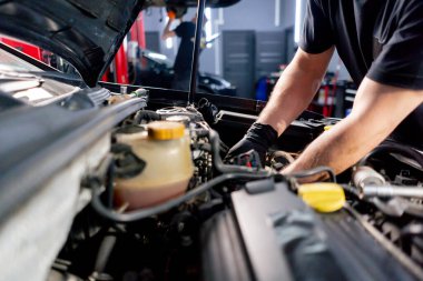 Bir araba servisi merkezinde siyah tişörtlü bir usta araç gereçleri kullanarak motor vidalarını söker yedek parçaların yerine yedek parçaları yerleştirir.