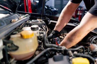 Bir araba servisi merkezinde siyah tişörtlü bir usta araç gereçleri kullanarak motor vidalarını söker yedek parçaların yerine yedek parçaları yerleştirir.