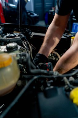 Bir araba servisi merkezinde siyah tişörtlü bir usta araç gereçleri kullanarak motor vidalarını söker yedek parçaların yerine yedek parçaları yerleştirir.