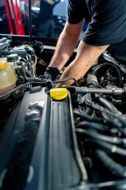 Bir araba servisi merkezinde siyah tişörtlü bir usta araç gereçleri kullanarak motor vidalarını söker yedek parçaların yerine yedek parçaları yerleştirir.
