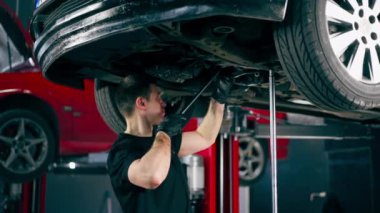 Bir benzin istasyonundaki oto tamirciyi kapat asansörde kaldırılan bir arabayı kontrol et, mekanik bir araçla arızaları düzelt motor alt gövdenin parçasını