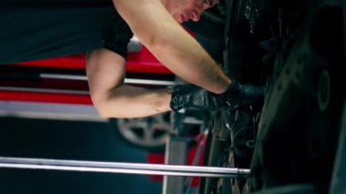 bir benzin istasyonunda bir oto tamirciyi kapatan dikey video asansörde kaldırılan bir arabayı kontrol eder, mekanik bir araçla arıza düzeltir motor alt gövdenin bir parçasıdır