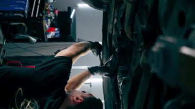 bir benzin istasyonunda bir oto tamirciyi kapatan dikey video asansörde kaldırılan bir arabayı kontrol eder, mekanik bir araçla arıza düzeltir motor alt gövdenin bir parçasıdır