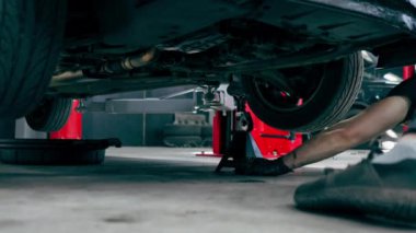 Bir araba servisinde asansörle yakın plan. Tekerlekle ilgili bir sorunu tamir etmek için bir makine. Paslı yayı olan bir tekerlek.