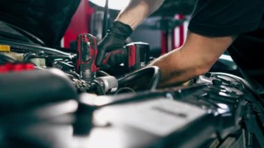 Siyah tişörtlü bir araba servisinin kapağını kapatın. Yedek parçaları değiştirmek için motor bölümündeki vidaları sökmek için matkap kullanın.