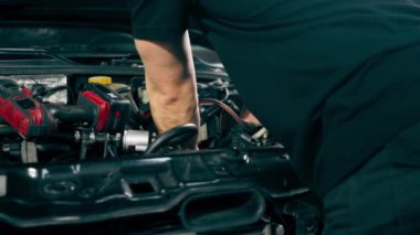 Siyah tişörtlü bir araba servisinin kapağını kapatın. Yedek parçaları değiştirmek için motor bölümündeki vidaları sökmek için matkap kullanın.