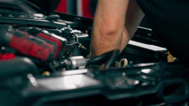 Bir araba servisi merkezinde siyah tişörtlü bir usta araç gereçleri kullanarak motor vidalarını söker yedek parçaların yerine yedek parçaları yerleştirir.
