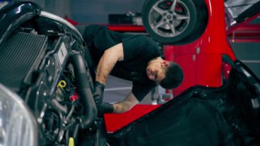 Siyah tişörtlü bir araba servisi ustasındaki dikey video yedek parçaların yerine arabanın motor bölümündeki vidaları sökmek için matkap kullanır.