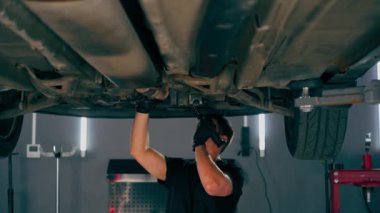 Benzin istasyonundaki oto tamircisi asansörde kaldırılan bir arabayı kontrol eder, mekanik bir araçla arıza düzeltir motor alt gövdenin bir parçasıdır