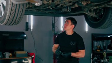 Benzin istasyonundaki oto tamircisi asansörde kaldırılan bir arabayı kontrol eder, mekanik bir araçla arıza düzeltir motor alt gövdenin bir parçasıdır