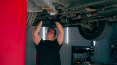 Benzin istasyonundaki oto tamircisi asansörde kaldırılan bir arabayı kontrol eder, mekanik bir araçla arıza düzeltir motor alt gövdenin bir parçasıdır