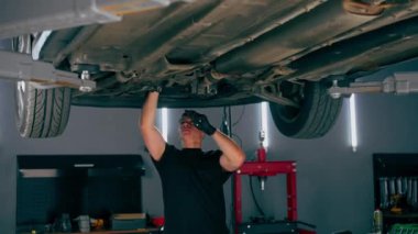 Benzin istasyonundaki oto tamircisi asansörde kaldırılan bir arabayı kontrol eder, mekanik bir araçla arıza düzeltir motor alt gövdenin bir parçasıdır