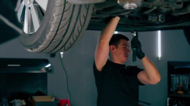 Benzin istasyonundaki oto tamircisi asansörde kaldırılan bir arabayı kontrol eder, mekanik bir araçla arıza düzeltir motor alt gövdenin bir parçasıdır