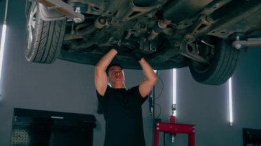 Benzin istasyonundaki oto tamircisi asansörde kaldırılan bir arabayı kontrol eder, mekanik bir araçla arıza düzeltir motor alt gövdenin bir parçasıdır