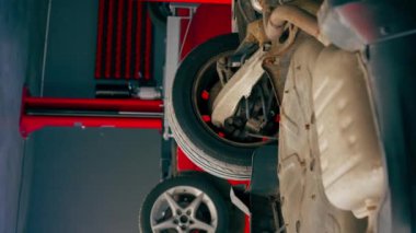 Bir otomobil tamircisi için özel bir mekanizma tarafından servis istasyonunda tekerlekleri yükseltilmiş siyah bir arabanın dikey görüntüsü.