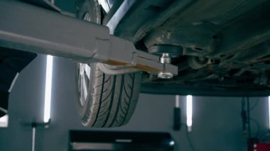 Bir otomobil tamircisi için özel bir mekanizma tarafından bir benzin istasyonunda tekerlekleri yükseltilmiş siyah bir arabanın yakın çekimi.