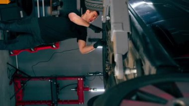 dikey video bir otomobil tamircisi asansörde kaldırılan bir arabayı kontrol eder, mekanik bir araçla arızaları düzeltir motor alt gövdenin bir parçasıdır