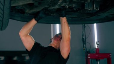 Benzin istasyonundaki oto tamircisi asansörde kaldırılan bir arabayı kontrol eder, mekanik bir araçla arıza düzeltir motor alt gövdenin bir parçasıdır