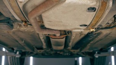 Benzin istasyonundaki oto tamircisi asansörde kaldırılan bir arabayı kontrol eder, mekanik bir araçla arıza düzeltir motor alt gövdenin bir parçasıdır