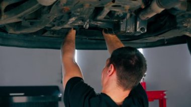 Benzin istasyonundaki oto tamircisi asansörde kaldırılan bir arabayı kontrol eder, mekanik bir araçla arıza düzeltir motor alt gövdenin bir parçasıdır