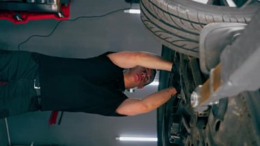 dikey video bir otomobil tamircisi asansörde kaldırılan bir arabayı kontrol eder, mekanik bir araçla arızaları düzeltir motor alt gövdenin bir parçasıdır