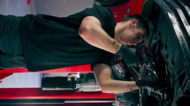 dikey video bir otomobil tamircisi asansörde kaldırılan bir arabayı kontrol eder, mekanik bir araçla arızaları düzeltir motor alt gövdenin bir parçasıdır