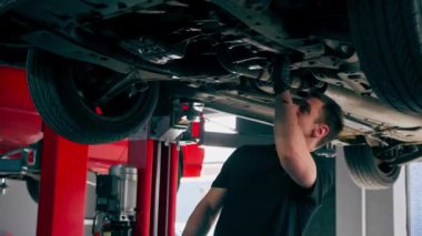 dikey video bir otomobil tamircisi asansörde kaldırılan bir arabayı kontrol eder, mekanik bir araçla arızaları düzeltir motor alt gövdenin bir parçasıdır