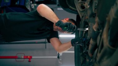 bir benzin istasyonunda bir oto tamirciyi kapatan dikey video asansörde kaldırılan bir arabayı kontrol eder, mekanik bir araçla arıza düzeltir motor alt gövdenin bir parçasıdır