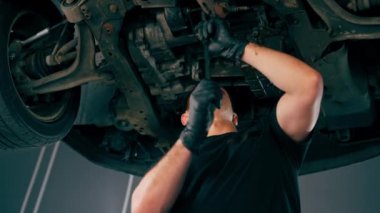 Benzin istasyonunda bir oto tamircisi düşük çekim asansörde kaldırılan bir arabayı kontrol eder, mekanik bir araçla arızaları giderir motor alt gövdenin bir parçasıdır