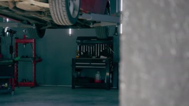 Bir otomobil tamircisi için özel bir mekanizma tarafından bir benzin istasyonunda tekerlekleri yükseltilmiş kırmızı arabanın yakın çekimi.