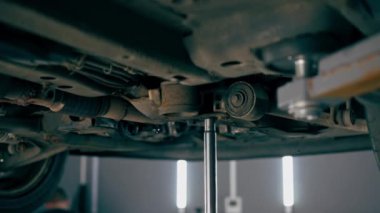 Bir benzin istasyonundaki oto tamirciyi kapat asansörde kaldırılan bir arabayı kontrol et, mekanik bir araçla arızaları düzelt motor alt gövdenin parçasını