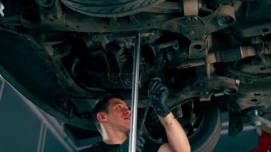 Benzin istasyonundaki oto tamircisi asansörde kaldırılan bir arabayı kontrol eder, mekanik bir araçla arıza düzeltir motor alt gövdenin bir parçasıdır