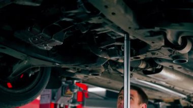 Benzin istasyonundaki oto tamircisi asansörde kaldırılan bir arabayı kontrol eder, mekanik bir araçla arıza düzeltir motor alt gövdenin bir parçasıdır