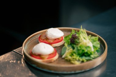 Profesyonel bir mutfakta, temiz metal bir masada, ahşap bir tabakta, domatesli ve mozzarella tostlu güzel bir salata.