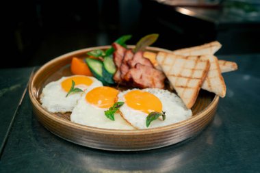 Profesyonel bir mutfakta, temiz metal bir masada, ahşap bir tabakta, kızarmış ekmekle pişirilmiş İngiliz kahvaltısı.