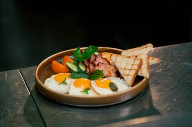 Profesyonel bir mutfakta, temiz metal bir masada, ahşap bir tabakta, kızarmış ekmekle pişirilmiş İngiliz kahvaltısı.