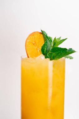 Beyaz arka planda yakın plan. Nane ve kurutulmuş portakalla süslenmiş sarı-turuncu karışımlı uzun cam bir bardak.