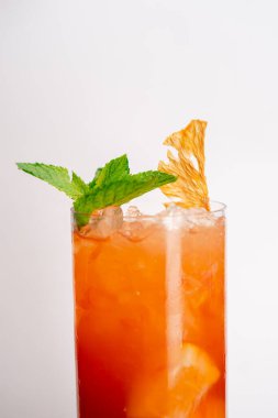 Beyaz arka planda yakın plan. Nane ve kurutulmuş portakalla süslenmiş sarı-turuncu karışımlı uzun cam bir bardak.