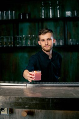 Barmen elinde bir bardak dolusu taze gül kokteyli tutuyor. Ekşi ve tatlı.