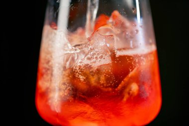Siyah bir zemin üzerinde şarap kadehinin makro çerçevesi. Cam bir cam parçasında ezilmiş buz var. Aperol Spritz bardağa dökülüyor.