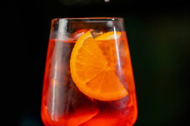 Siyah arka planda bir şarap kadehinin yakın plan görüntüsü. Cam camda, portakal rengi Aperol Spritz ile ezilmiş buz var. Camda tam yoğunlaşma.